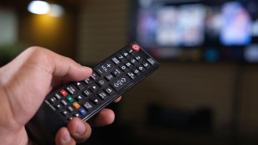 テレビのリモコンを持った手と遠くの画面