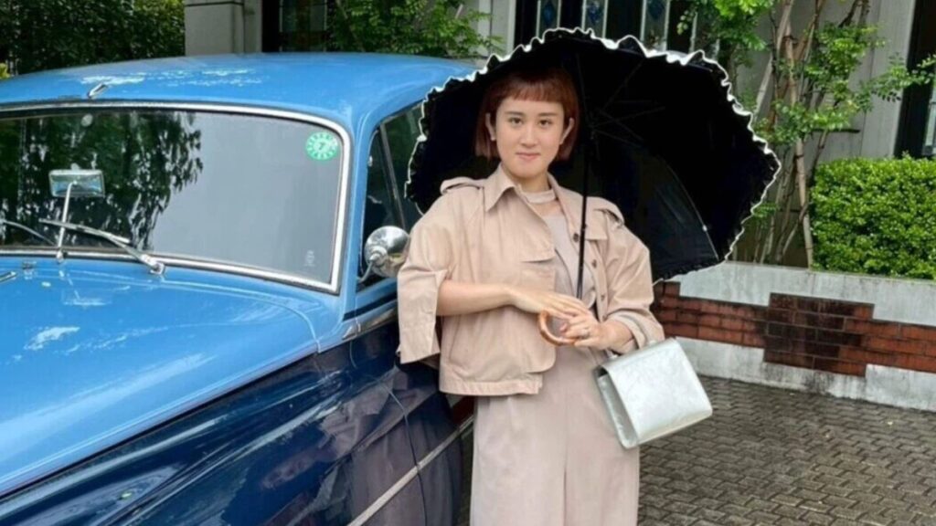 青い車の前に傘を持って立つ忠犬立ハチ高の王坂